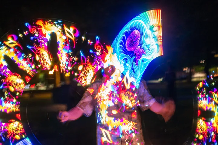 A flow artist spinning bright multicolor LED fans after dark at the jam
