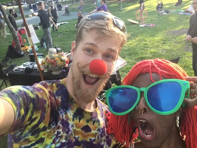 Two Taco Tuesday Flow Jam regulars making faces at the camera while wearing a clown nose, red yarn wig, and oversized green sunglasses